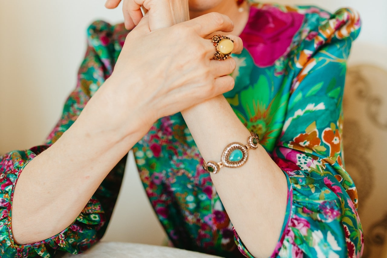 a woman in a patterned blouse wearing a gemstone bracelet and fashion ring