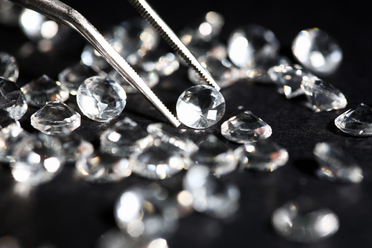 A jeweler observes a round-cut diamond using a specialized tool among an array of other round-cut diamonds in a black background