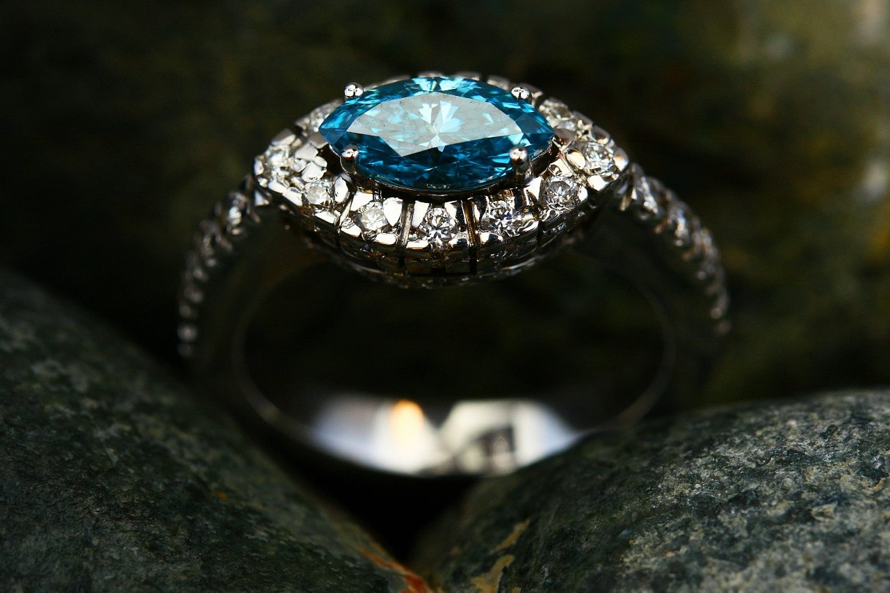 A close-up of a distinctive halo engagement ring with a marquise shape blue topaz center stone, delicately displayed between two stones.