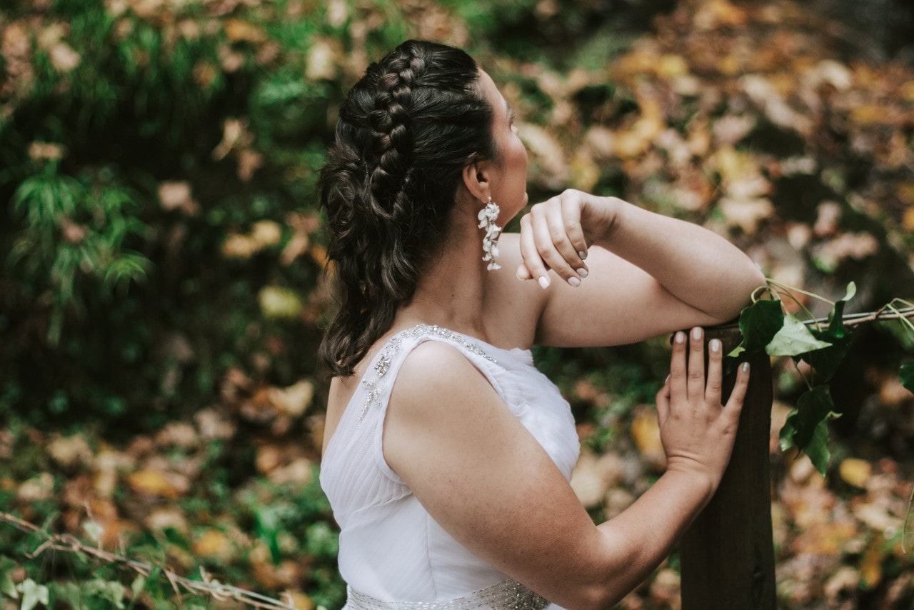 a bride resting against a post and looking away into the forest during the fall