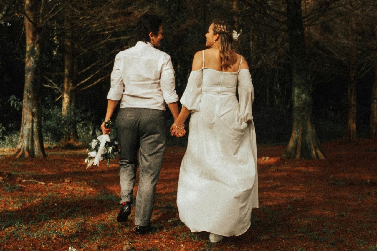 two brides walking through a forest during the fall