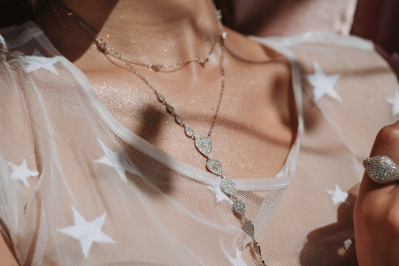 a woman’s neckline adorned with layered silver and diamond necklaces