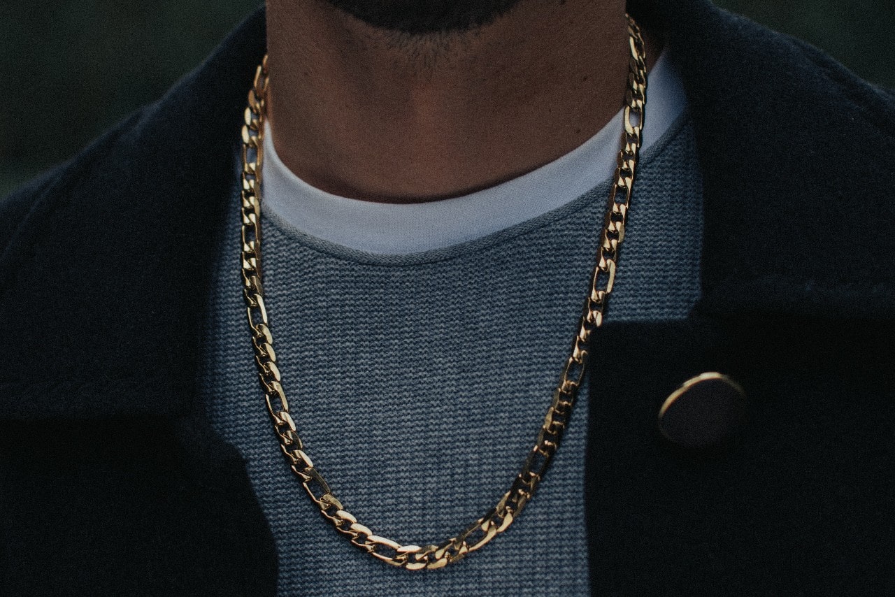 a close up image of a man’s neckline wearing a gray sweater and gold chain