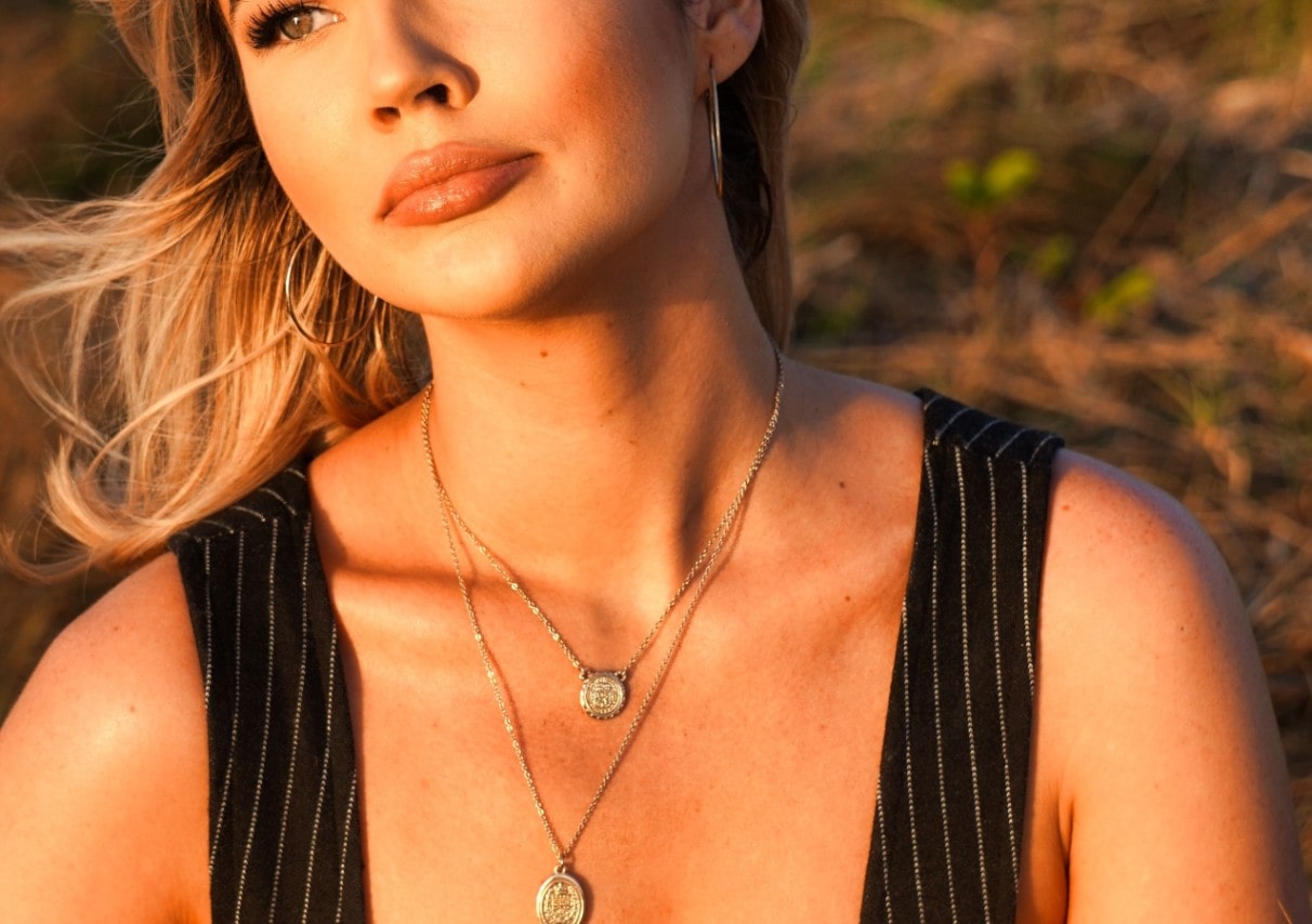 a woman watching a sunset wearing two medallion pendant necklaces.