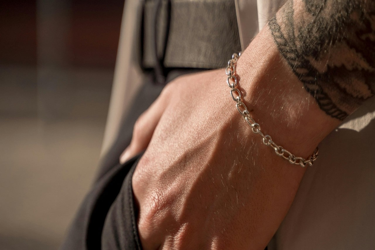 a man’s hand in his pocket wearing a silver chain bracelet