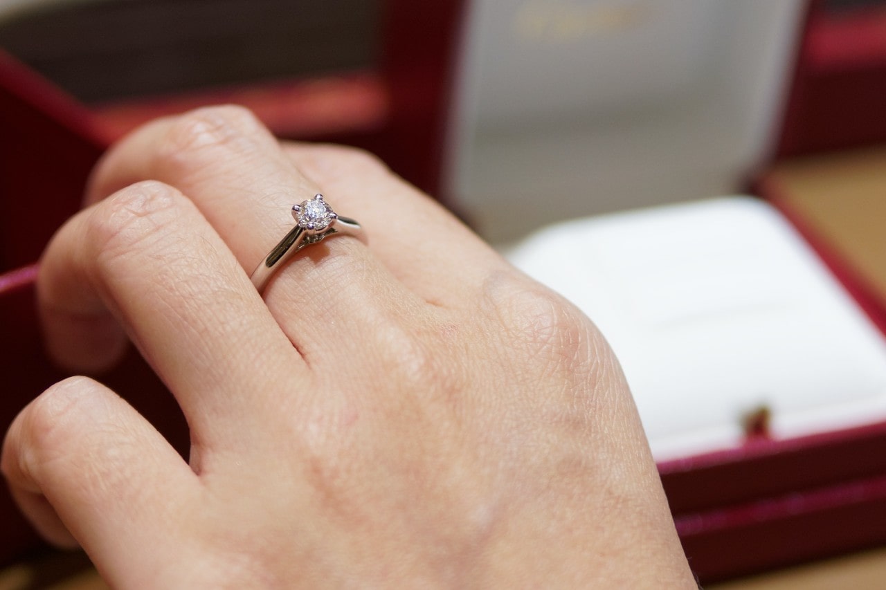 A close-up of a woman’s hand, wearing a solitaire diamond ring.