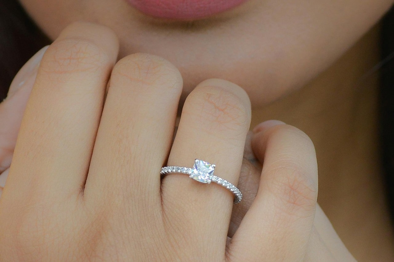 A close-up of a woman resting her hand on her chin, wearing a side stone diamond ring.