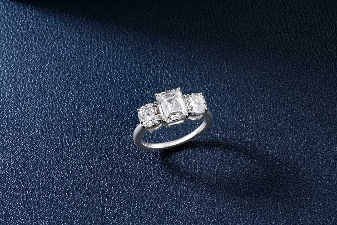 A close-up of an elegant three stone ring on a navy blue leather backdrop.