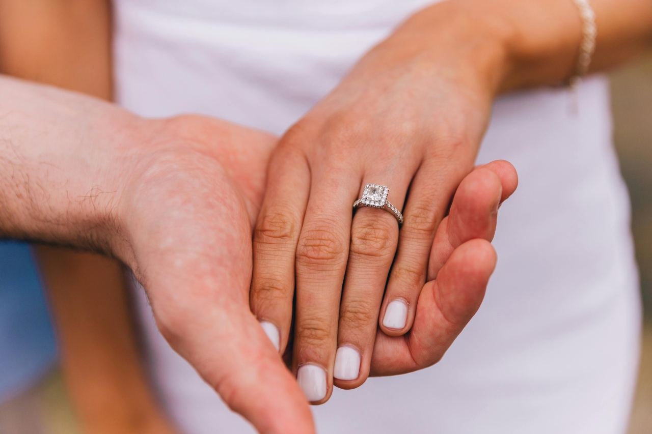 A close-up of a woman’s hand in a man’s, her finger adorned with an ornate halo ring.