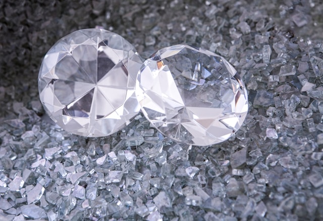 A close-up of two elegant round cut diamonds, displayed atop smaller diamond shavings.