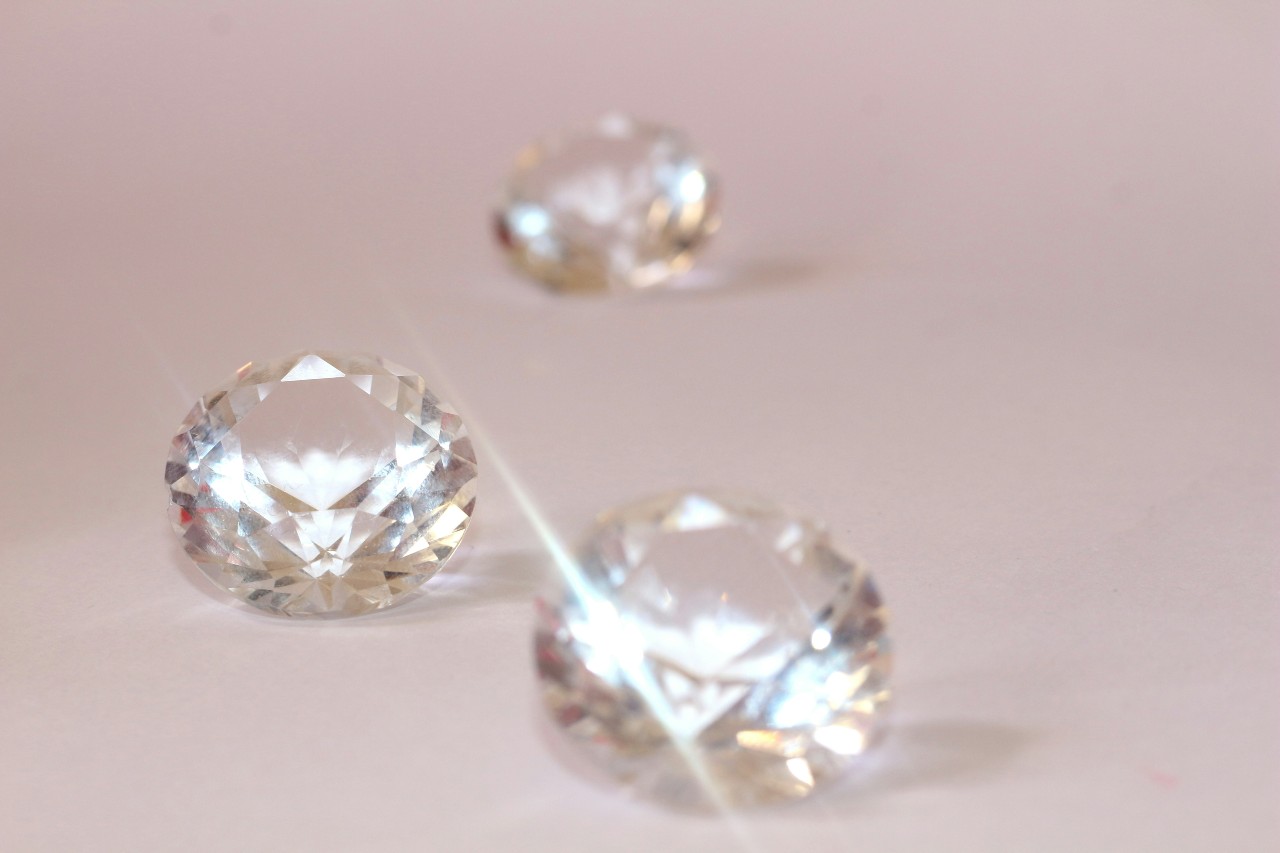 A close-up of three glistening round cut diamonds on a pale pink backdrop.