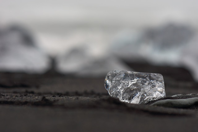 A close-up of an uncut diamond resting on a patch of soil.