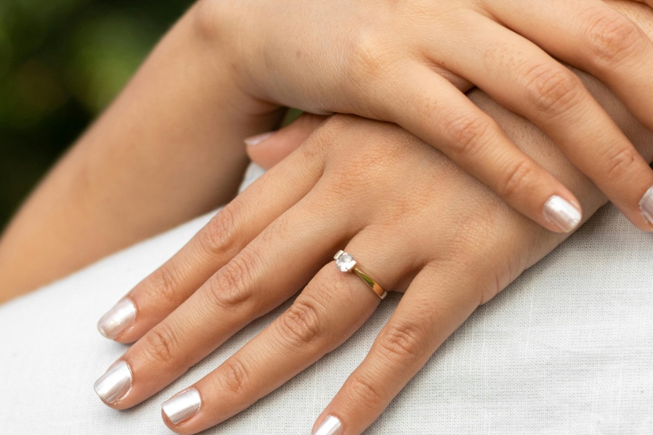 a woman’s hands resting on a man’s back, one of her fingers donning a solitaire engagement ring