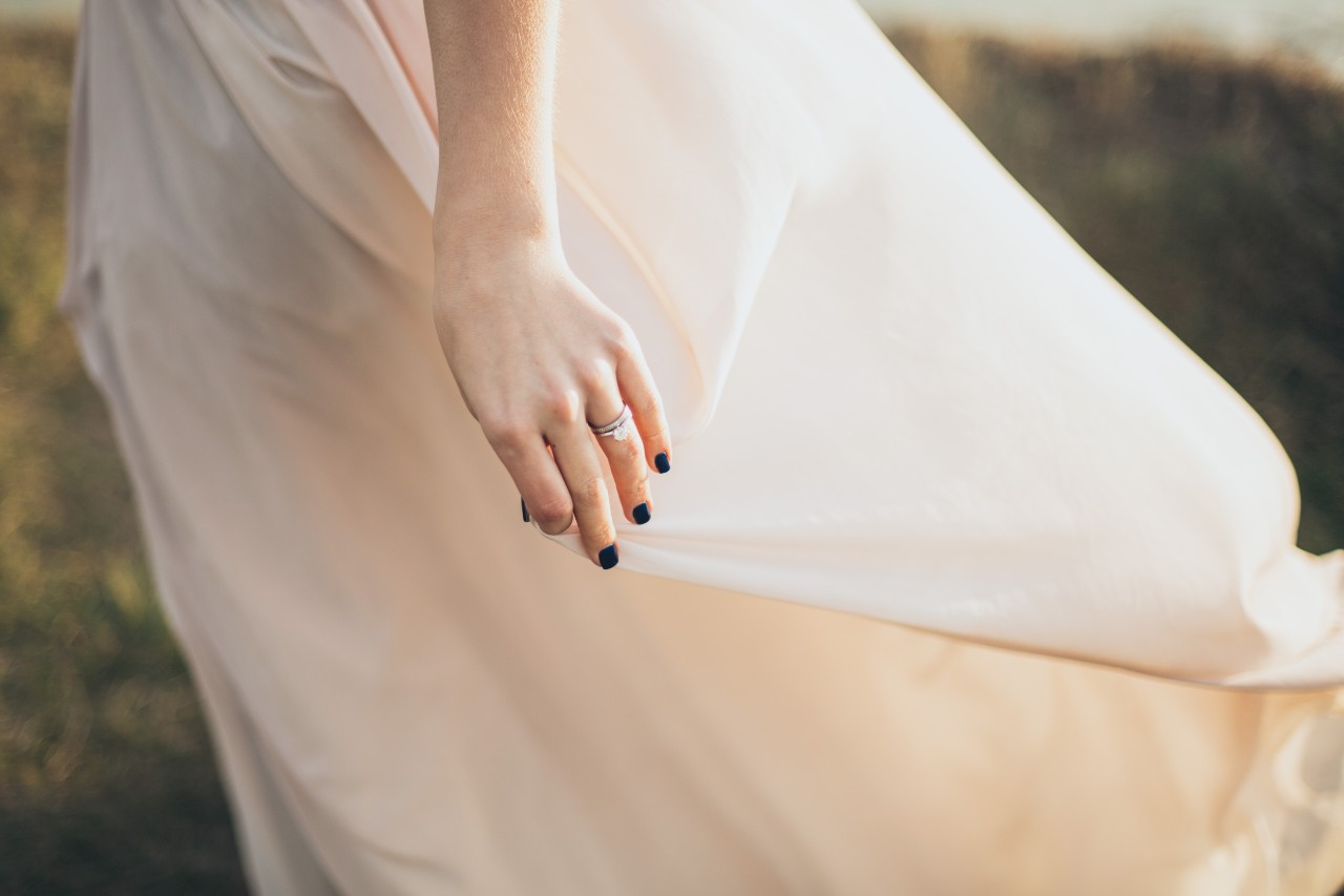 A bride standing in a field with a view on her engagement ring and wedding band