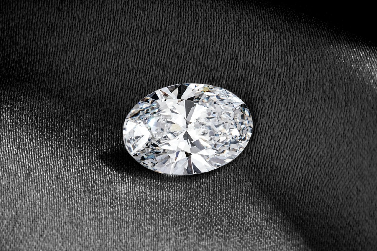 A stunning oval-cut diamond on a dark fabric background.