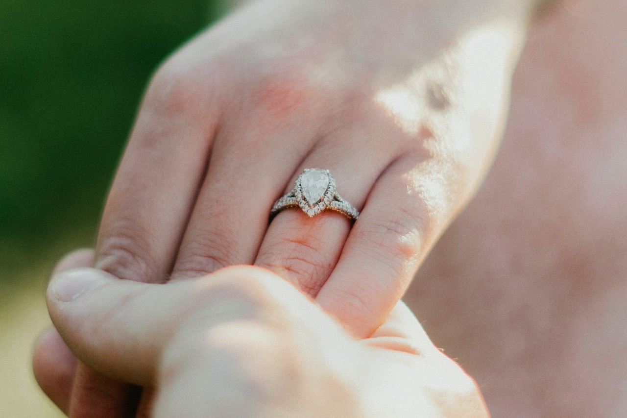 A man holding a woman’s hand that is adorned with a pear shaped halo engagement ring.